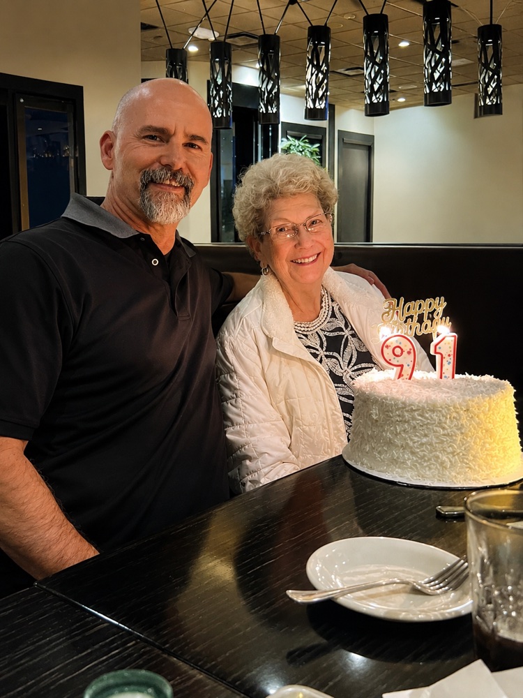 John Stuart with his mother at her 91st birthday dinner, her cake topped with '91' candles